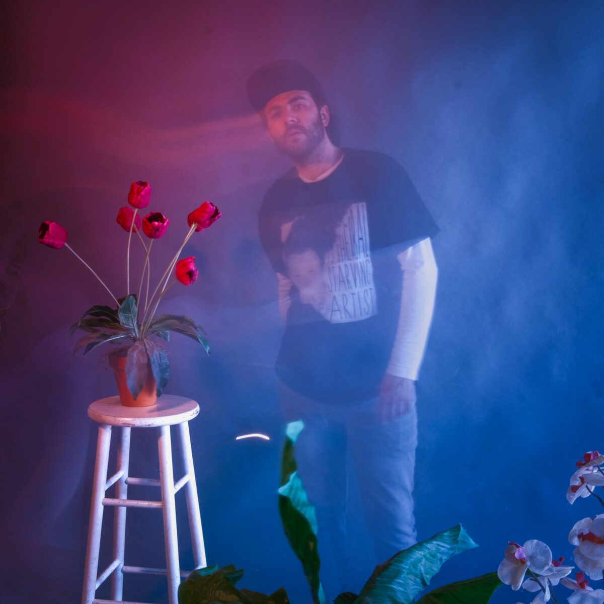 Kenny Moreno sitting beside a vase of flowers against a blue backdrop